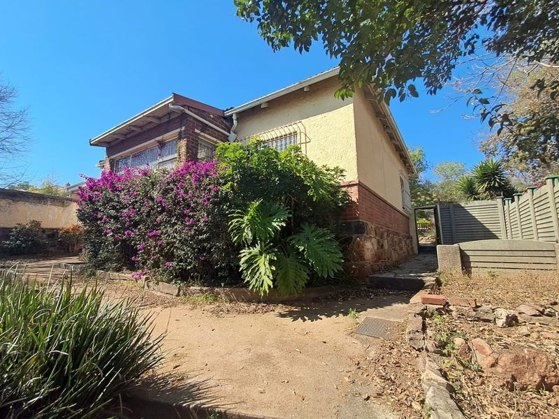 Front elevation of a character home featuring a mix of brick and plastered finishes, security bars, and established garden beds.