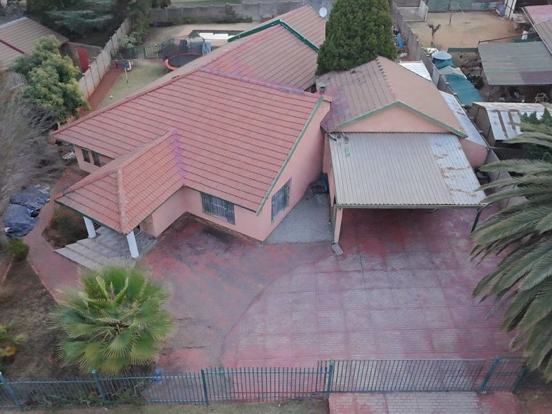 Aerial view of a residential property featuring a tiled roof house, paved driveway, carport, and perimeter fencing.