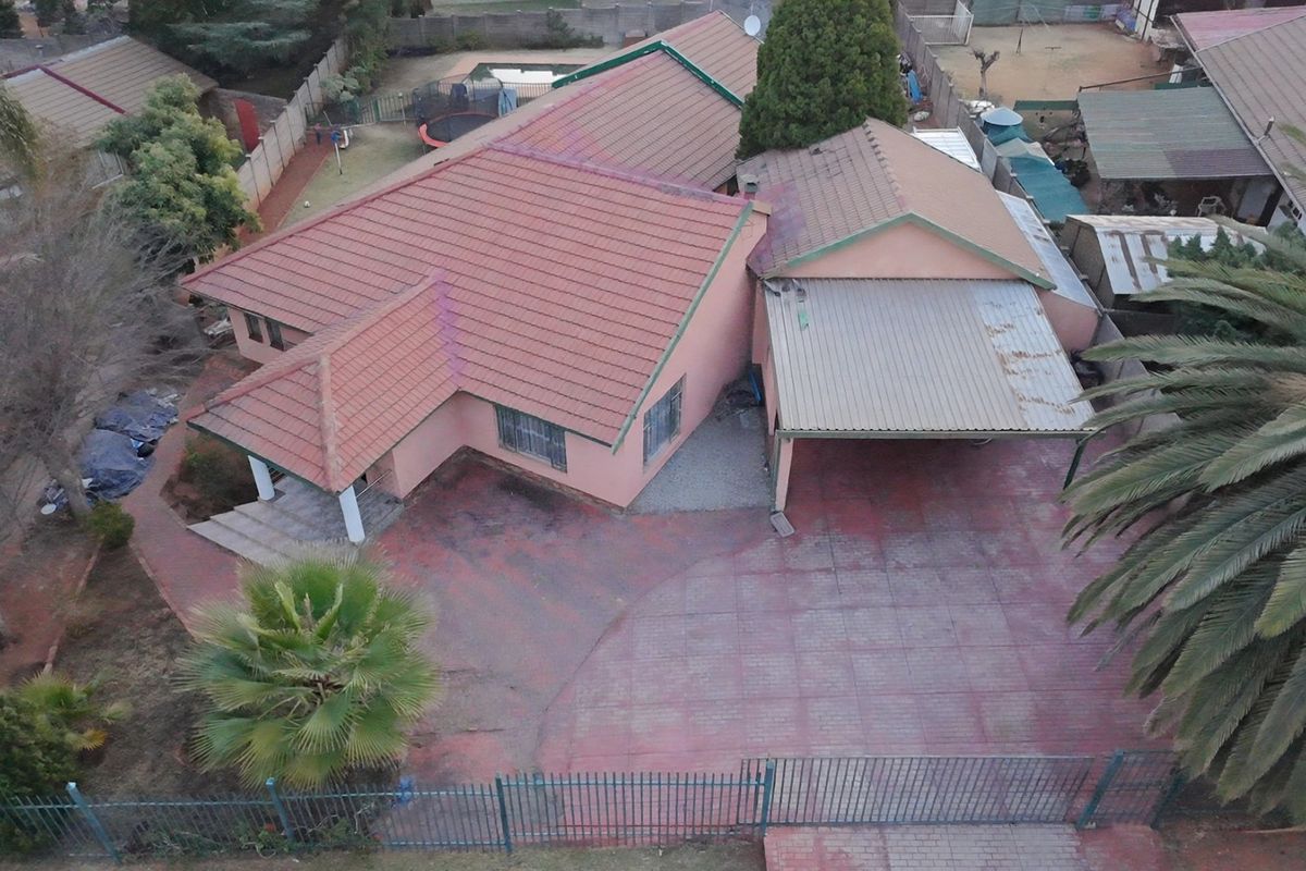 Aerial view of a residential property featuring a tiled roof house, paved driveway, carport, and perimeter fencing.