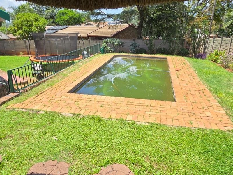 Outdoor swimming pool area featuring a brick surround, perimeter wall, and metal fencing, currently requiring maintenance and pool water treatment.