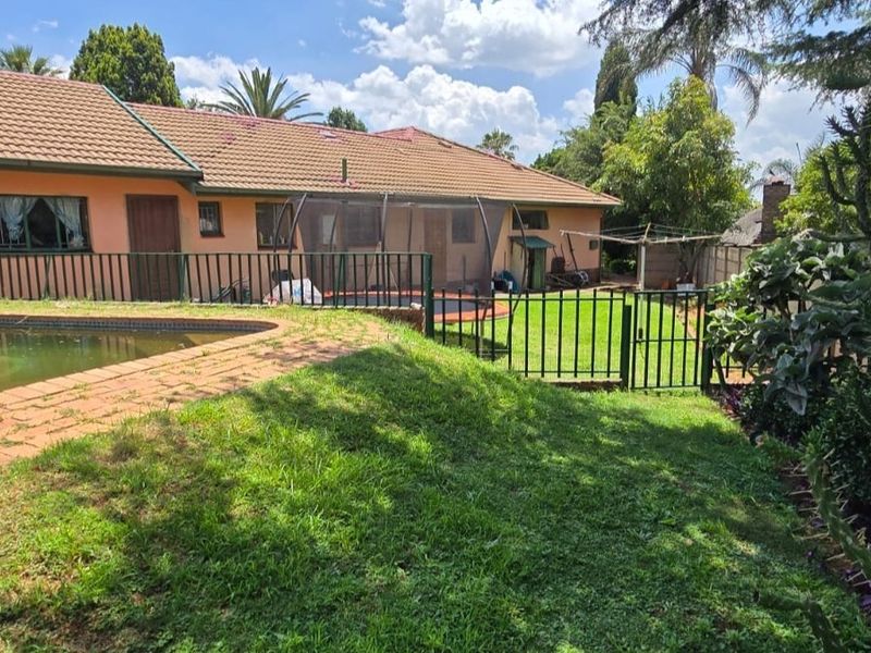 Rear view of the property featuring a swimming pool, lawn area, and perimeter metal fencing with a tiled roof structure.