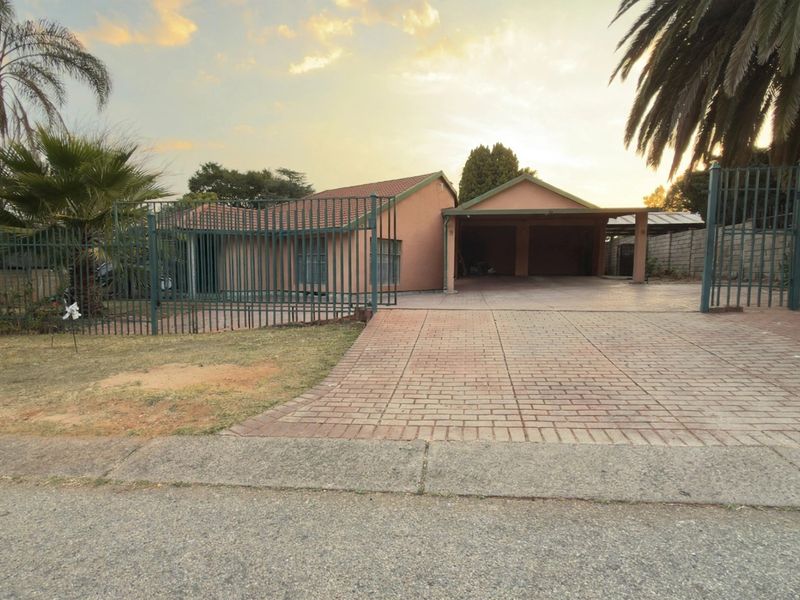Front view of a single-story house featuring a paved driveway, double carport, and secure metal perimeter fencing.