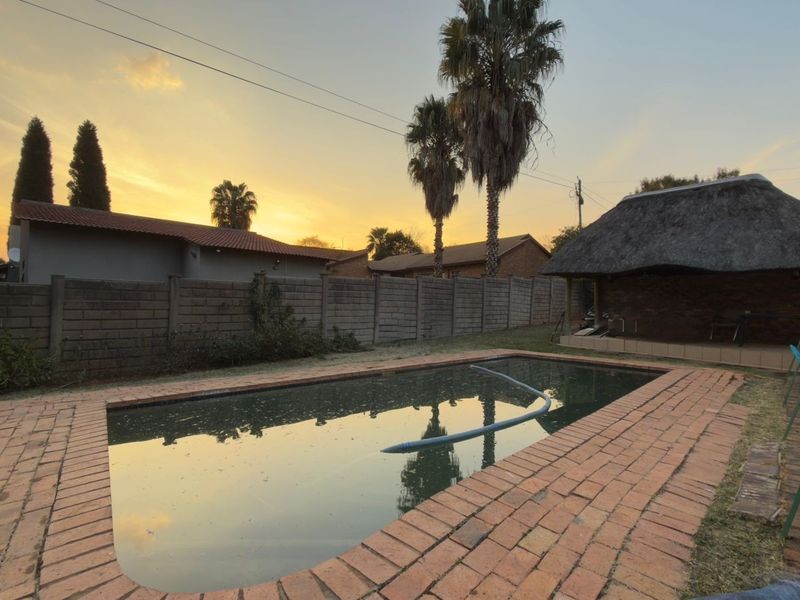 Outdoor pool area featuring a swimming pool with brick coping and an adjacent thatch lapa structure, set within a walled garden.
