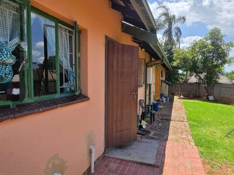 Rear exterior view of the property featuring brick paving, a garden area, and a boundary wall, showing signs of exterior wall maintenance required.