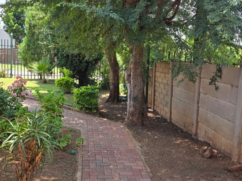 A landscaped garden area featuring a paved walkway, mature trees, and a secure precast concrete boundary wall.