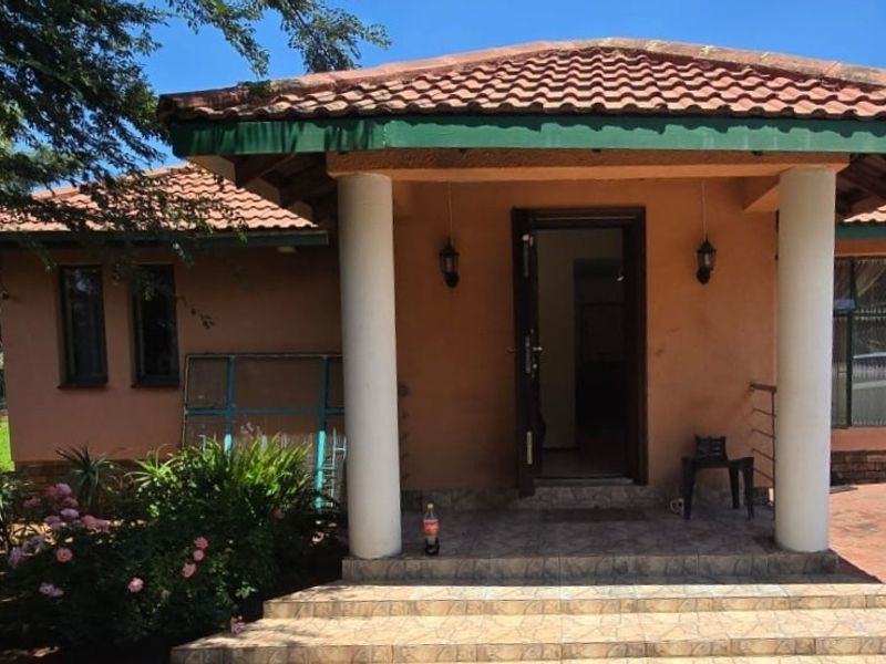 Front entrance of a single-story house featuring a covered porch with concrete columns, tiled steps, and a paved driveway area.