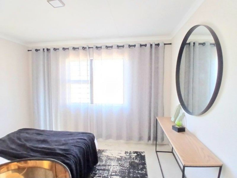 A bright and neutral bedroom featuring a large window with curtain rod and recessed ceiling lighting.