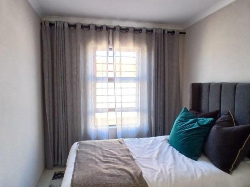 A well-maintained bedroom featuring neutral wall tones, a window with security bars, and modern curtain fixtures.