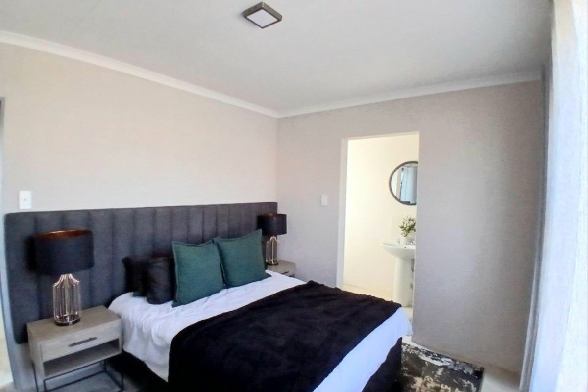 A well-maintained bedroom featuring a modern upholstered headboard, neutral wall tones, and direct access to an en-suite bathroom.