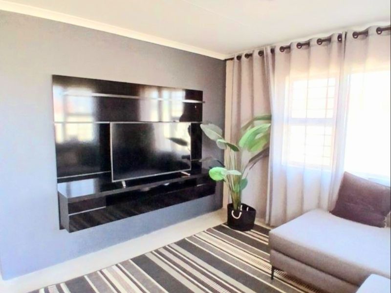 A well-maintained living room featuring a modern built-in media console and large window with security bars, providing a functional and comfortable living space.