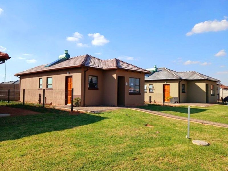 A view of the rear exterior of the property featuring a well-maintained lawn, paved walkways, and tiled roof structures with solar water heaters.
