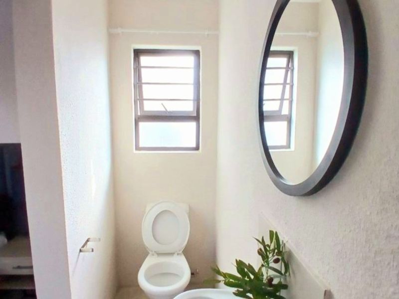 A compact bathroom featuring a pedestal basin, toilet, and louvered window, providing functional utility in a simple, clean layout.