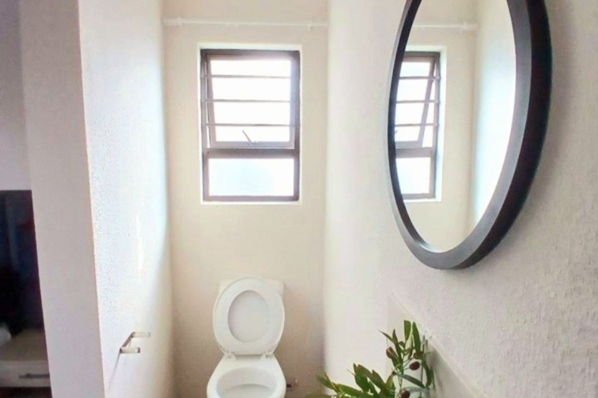 A compact bathroom featuring a pedestal basin, toilet, and louvered window, providing functional utility in a simple, clean layout.
