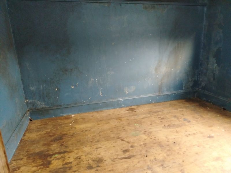 An empty room featuring timber flooring and blue painted walls showing significant signs of wear and surface deterioration.