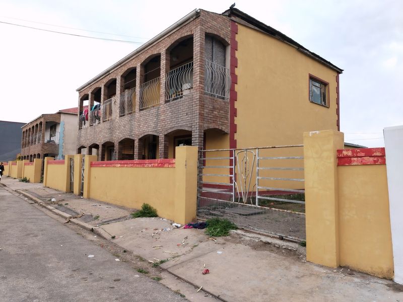 Two-story commercial building featuring a brick facade with arched balconies, enclosed by a perimeter wall and metal gate, showing signs of exterior wear.