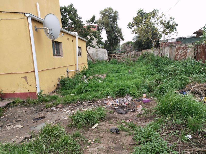 Rear exterior view of the commercial property showing the building facade, downpipe, satellite dish, and an unmaintained yard area with overgrown grass and debris.
