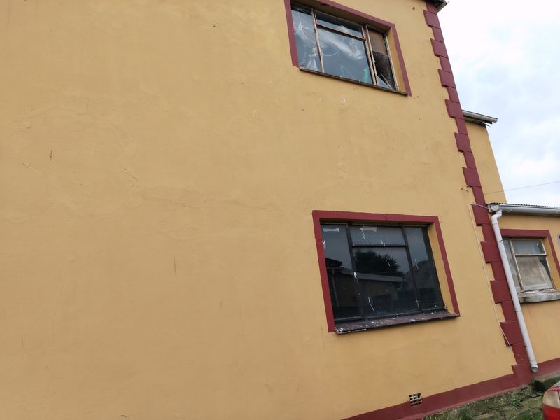 Exterior view of a commercial building facade showing significant wear, including damaged window frames and cracked plasterwork requiring maintenance.