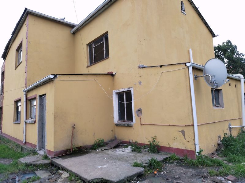Rear exterior view of a commercial building showing yellow painted facade, metal window frames, and a concrete patio area requiring maintenance.