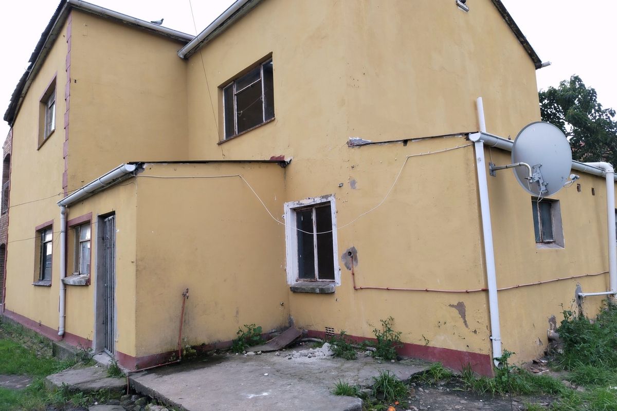 Rear exterior view of a commercial building showing yellow painted facade, metal window frames, and a concrete patio area requiring maintenance.