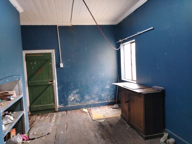 A vacant utility space featuring timber flooring and a tongue and groove ceiling, requiring significant refurbishment and cosmetic repairs to the walls and floors.