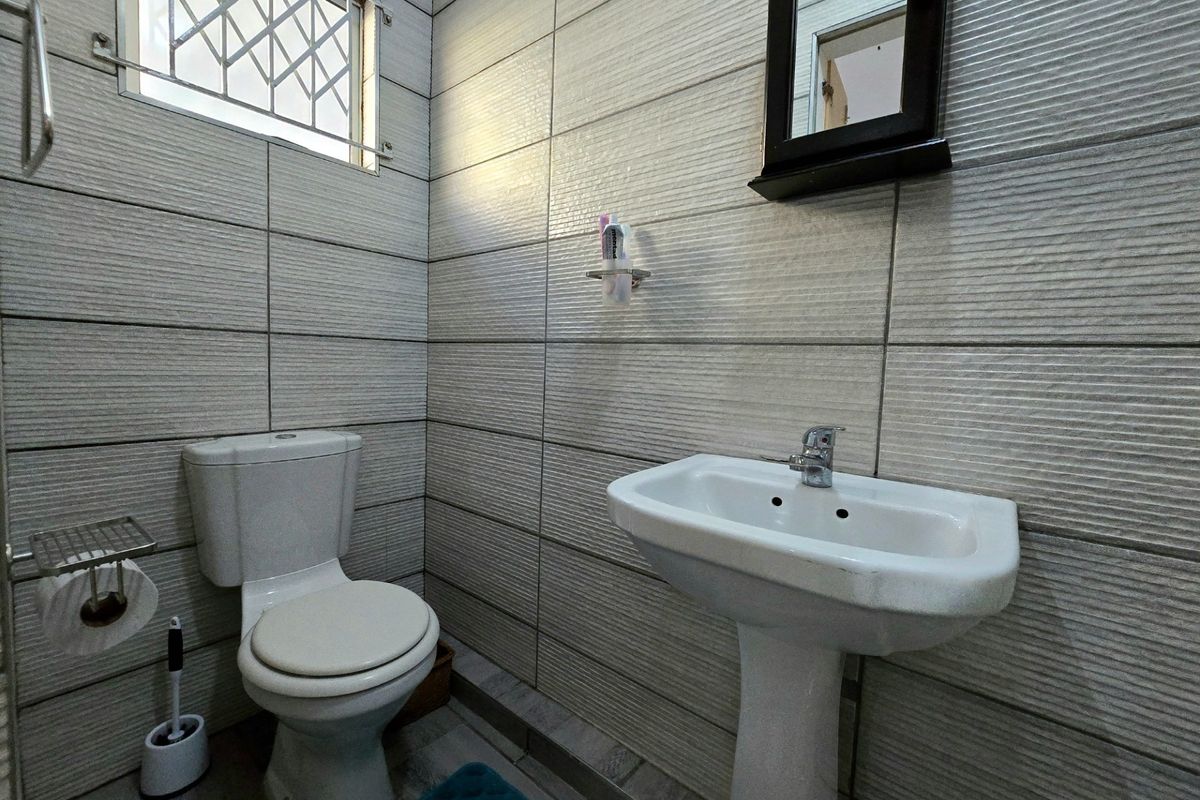 A compact, well-maintained bathroom featuring tiled walls, a pedestal basin, and a standard toilet with security bars on the window.