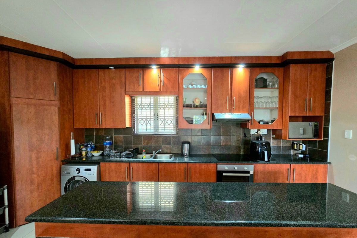 A functional kitchen featuring dark granite countertops, wood-finish cabinetry, a built-in oven, hob, extractor fan, and a tiled backsplash.