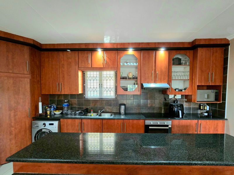 A functional kitchen featuring dark granite countertops, wood-finish cabinetry, a built-in oven, hob, extractor fan, and a tiled backsplash.