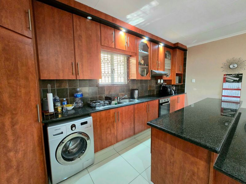 A functional kitchen featuring warm-toned wooden cabinetry, granite countertops, a breakfast bar, and integrated appliances including an oven and extractor fan.