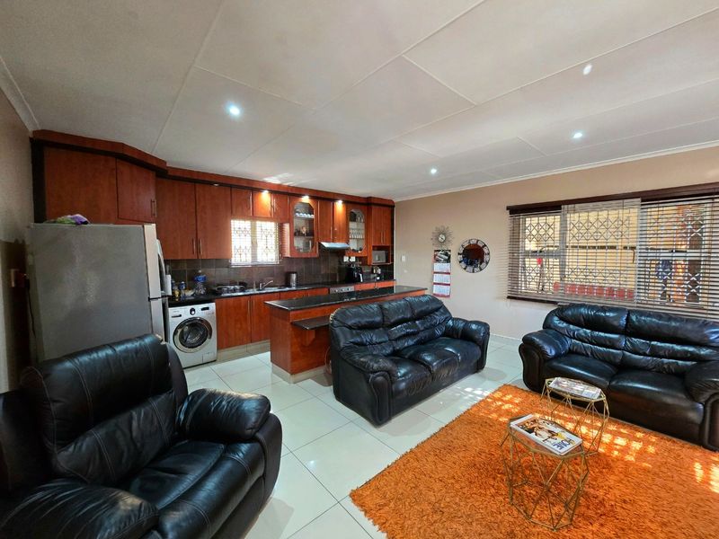 Open-plan living area featuring a kitchen with wooden cabinetry, granite countertops, and integrated appliances, flowing into a comfortable lounge space with tiled flooring.