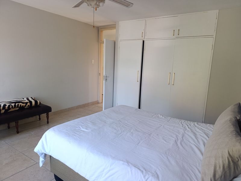 A bedroom featuring tiled flooring, a ceiling fan, and ample built-in cupboard storage space.