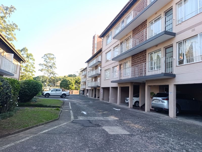 Exterior view of a multi-story apartment complex featuring brick facade, private balconies, and ground-level covered parking bays.