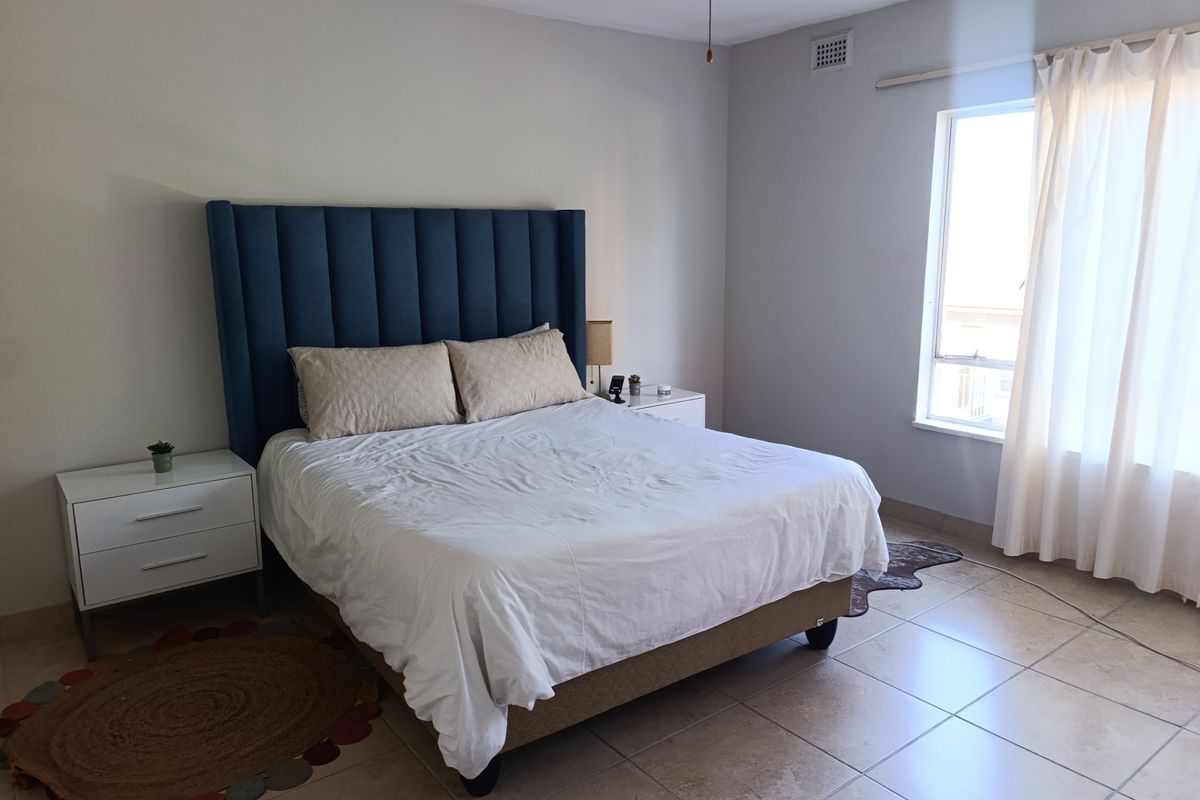 A spacious bedroom featuring neutral tiled flooring, a ceiling fan, and natural light from a large window.
