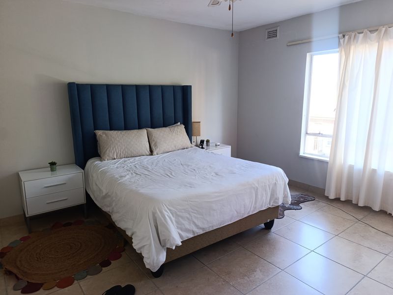 A spacious bedroom featuring neutral tiled flooring, a ceiling fan, and natural light from a large window.