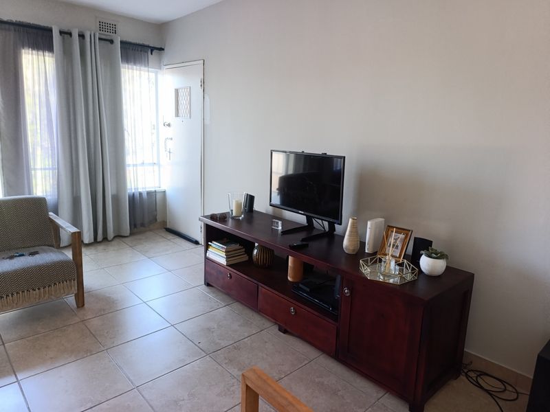 A living room area featuring neutral tiled flooring, a security entrance door, and a high-level ventilation grille.