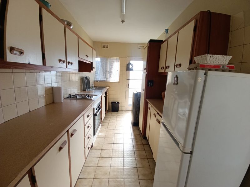 A functional galley-style kitchen featuring dated cabinetry, laminate countertops, a gas hob, and tiled flooring with direct access to the exterior.