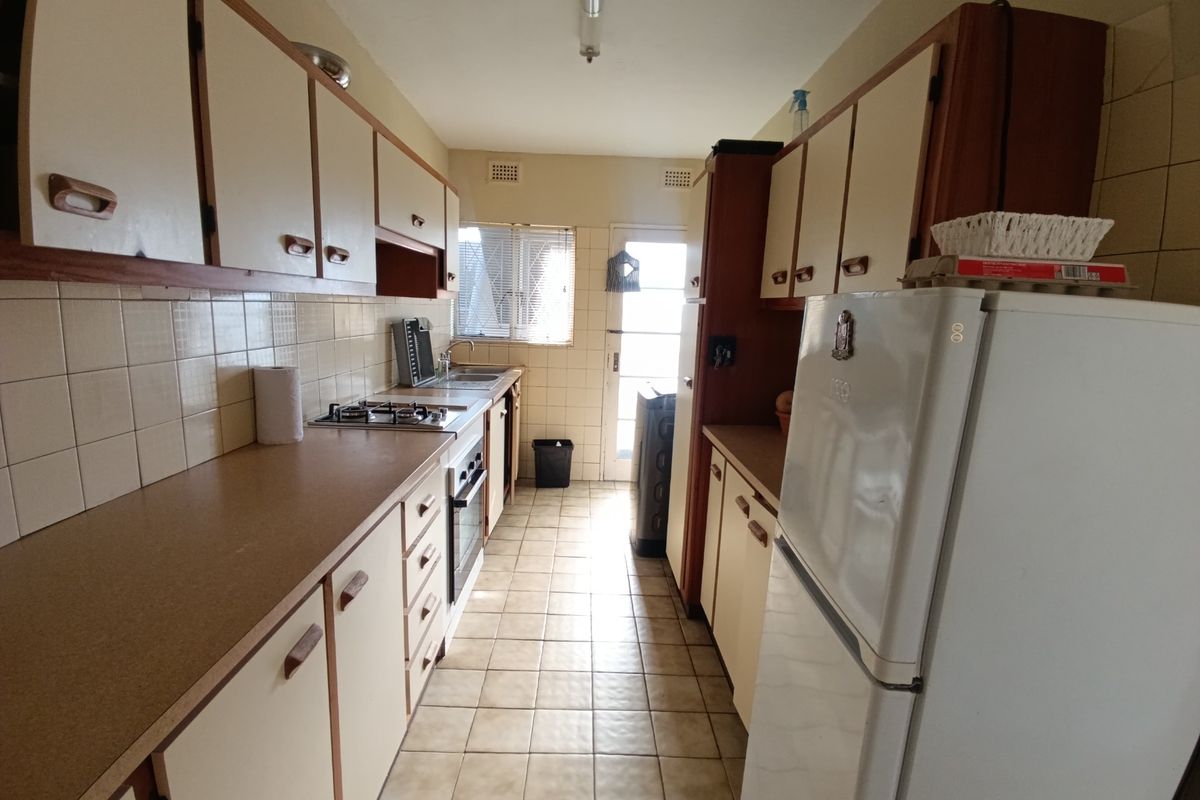 A functional galley-style kitchen featuring dated cabinetry, laminate countertops, a gas hob, and tiled flooring with direct access to the exterior.