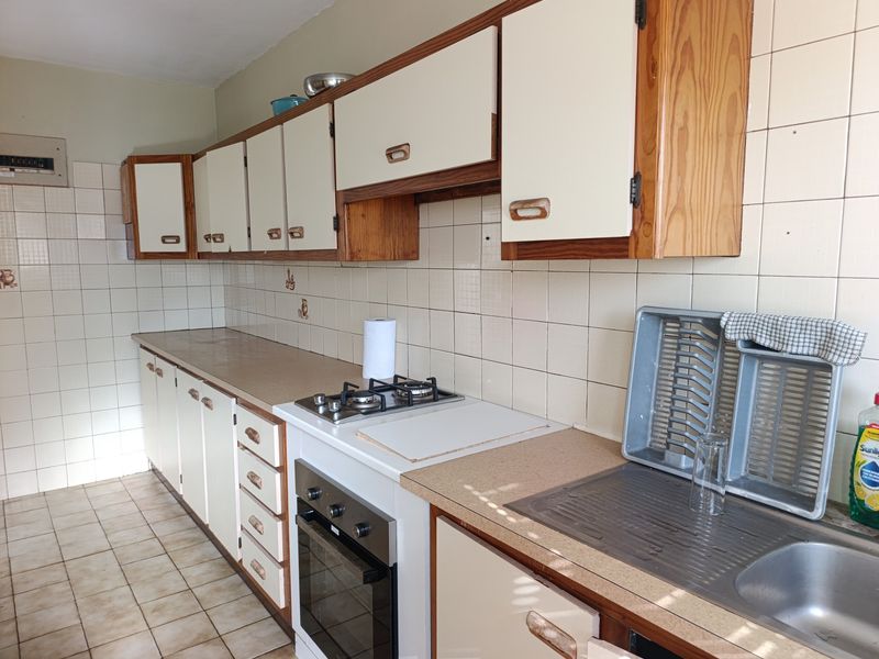 A functional kitchen featuring dated cabinetry, laminate countertops, a built-in oven with gas hob, and tiled splashbacks.