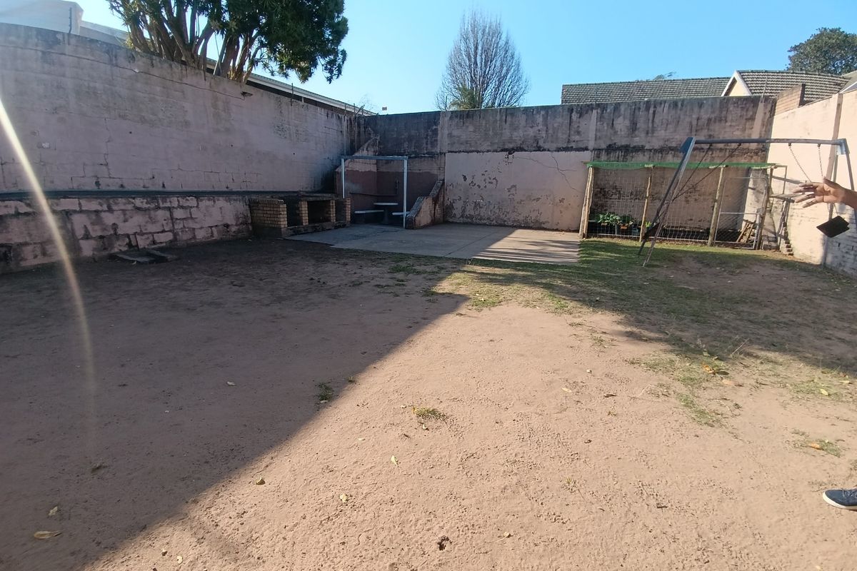 A spacious rear courtyard featuring high perimeter boundary walls, a built-in brick braai, and a paved patio area, offering potential for landscaping.