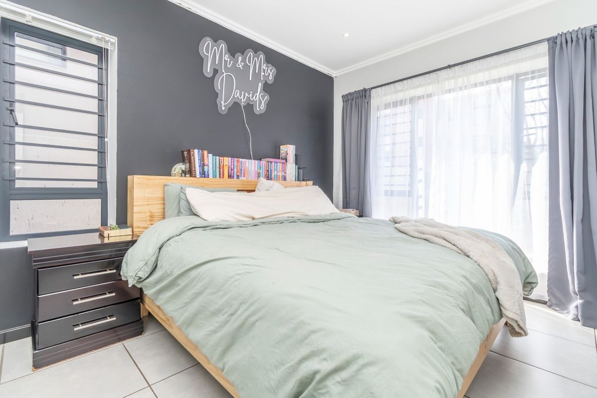 A well-lit bedroom featuring tiled flooring, a sliding glass door with curtains, and a louvered window, finished with modern cornicing and recessed lighting.