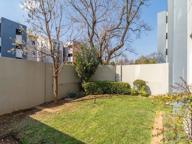 A private rear garden area featuring a small lawn, established trees, and high boundary walls for privacy.