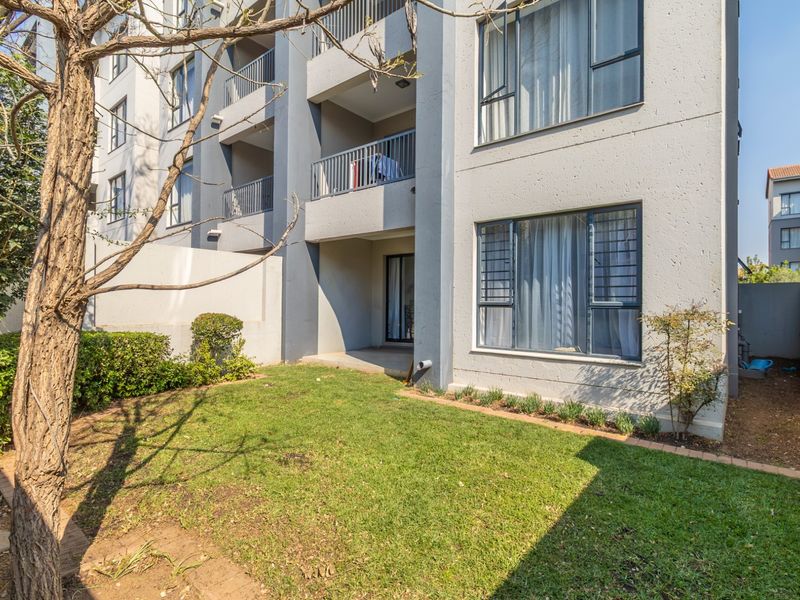 Ground floor apartment exterior featuring a private garden area, paved borders, and access to a balcony with sliding doors and security bars.