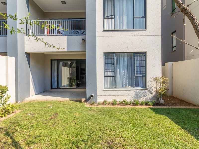 Rear view of the apartment featuring a ground floor patio, a small private lawn, and an upper-level balcony with metal railings.