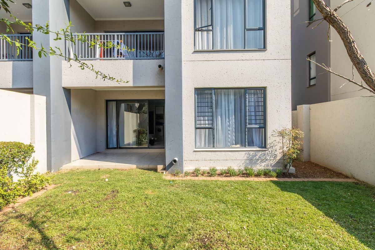 Rear view of the apartment featuring a ground floor patio, a small private lawn, and an upper-level balcony with metal railings.