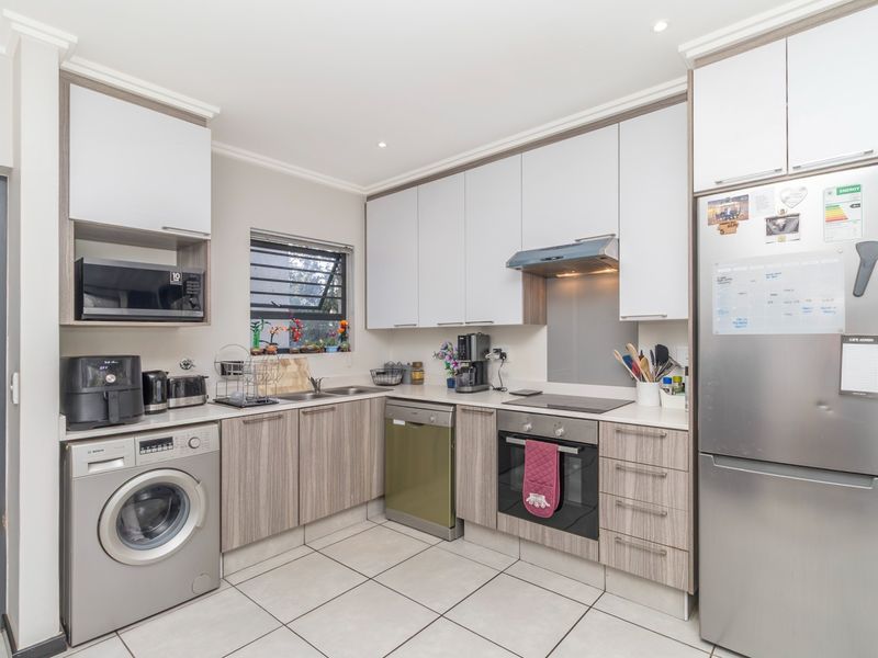 Modern kitchen featuring light wood-grain cabinetry, stone-look countertops, integrated appliances, and tiled flooring, offering a clean and functional workspace.
