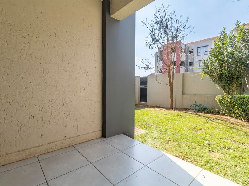 A covered patio area with tiled flooring, overlooking a private garden space with a boundary wall.