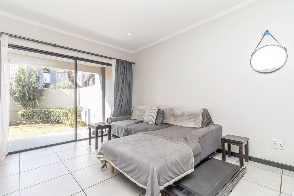 A bright living room featuring large sliding glass doors that open to a private garden area, complemented by neutral tiled flooring.