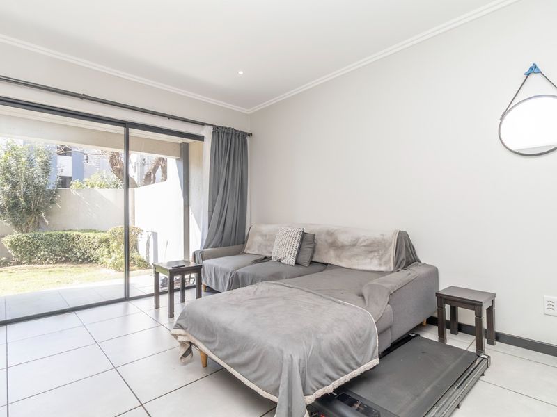 A bright living room featuring large sliding glass doors that open to a private garden area, complemented by neutral tiled flooring.