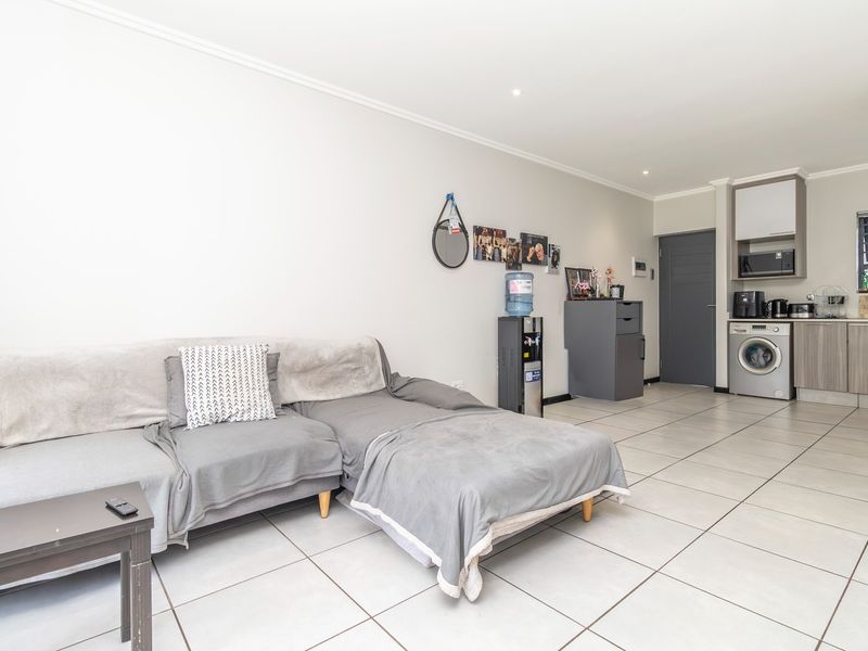 Open-plan living area featuring tiled flooring, recessed lighting, and a compact kitchen with built-in cabinetry and integrated laundry appliances.