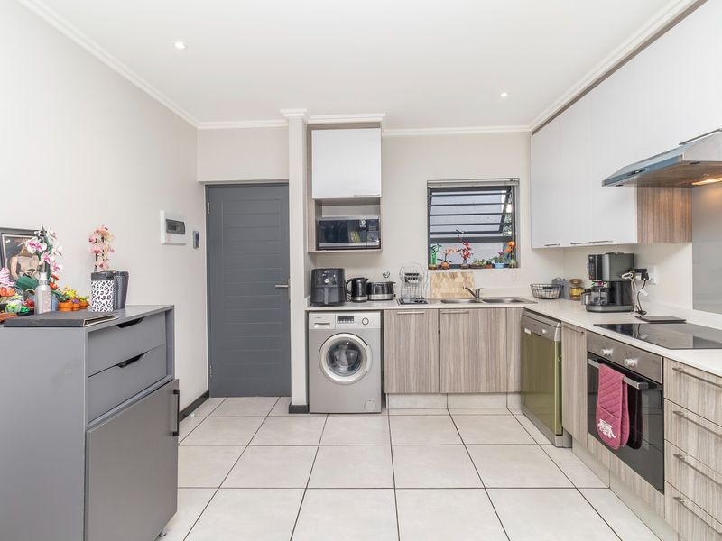 Modern kitchen featuring wood-grain cabinetry, integrated oven, electric cooktop, extractor fan, and tiled flooring with dedicated space for laundry appliances.