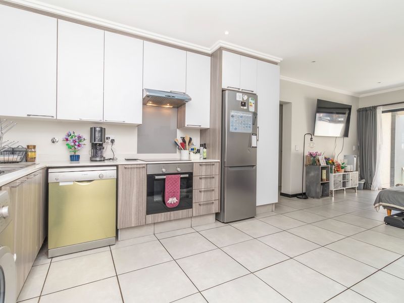 Modern open-plan kitchen and living area featuring sleek cabinetry, integrated appliances, tiled flooring, and direct access to an outdoor patio space.